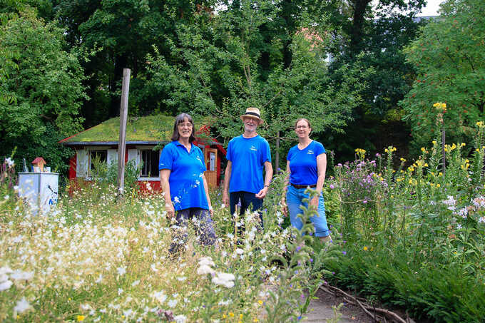 Drei Personen stehen in einem naturnahen Garten